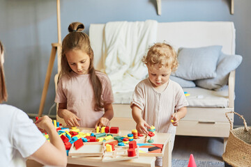 Obraz na płótnie Canvas Studying through play and toys. Smart educational lesson. Concentrated girls sisters learning together with wooden educational toys playing together at homer interior.
