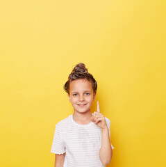 Charming positive child girl with shampoo on wet hair wearing white T-shirt standing isolated over yellow background pointing finger up showing copy space for advertisement.