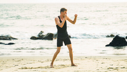 young man boxing on the coastline in a black sportswear
