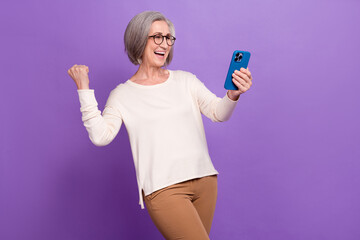 Fototapeta premium Photo of excited business lady fist up achieve successfully got her smartphone latest model best options isolated on purple color background