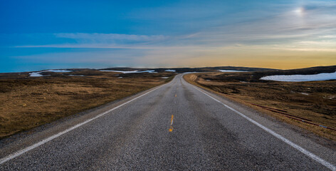 Asphalt road in beautiful tundra landscape with dry grass and some snow