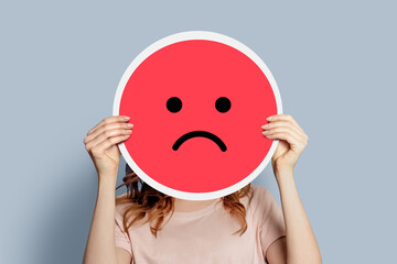 Sad emoji. Girl holds a yellow emoticon with sad face isolated on a gray background. unhappy emoji