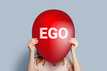 ego concept. Girl holding a balloon with the word EGO isolated on a gray background