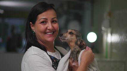 Portrait of a Happy woman drying Small Dog with towel inside Pet Shop. Female Small Business owner...
