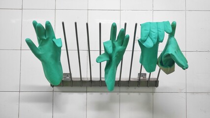 Green rubber gloves hanged on the hanger which stick on white tiled wall