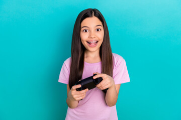 Portrait of excited little child girl hold gamepad joystick sony playstation have fun game addiction isolated on cyan color background