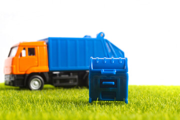 Photo of toy garbage truck with blue colored container on green lawn and white background.