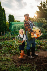 Grandfather and his granddaughter smiling after harvesting vegetables