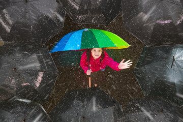 Girl under colorful umbrella in dark crowd.