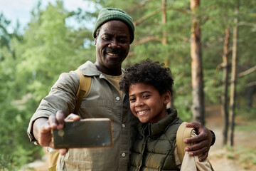 African American dad making selfie portrait with his son on smartphone during their hiking