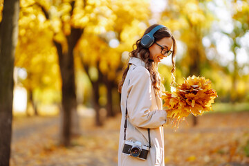 Smiling woman with retro camera and headphones enjoys sunny weather in autumn park. Autumn...