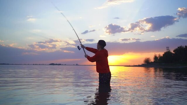 a fisherman casts a fish bait into the sea and spins a reel on a fishing rod against the background of a sunset