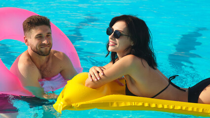 Aerial view of young woman and woman relaxing on inflatable ring in resort pool. Couple enjoying holidays at luxury resort.