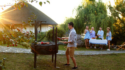 A man prepares food in nature. A group of young people gathered for a barbecue. Friends have fun, cook food, drink alcohol. They gathered in nature on a sunny day.