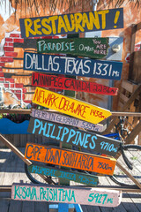Close-up of colorful mileage signs for multiple locations at a restaurant on Grand Cayman in the...