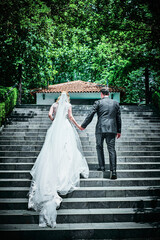 A bride and groom walk up the stairs holding hands.