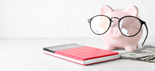 Piggy bank with eyeglasses, money and calculator on light background with space for text