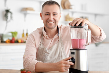 Mature man making fruit smoothie with blender in kitchen