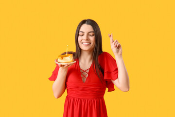 Beautiful young woman with sweet birthday cake making wish on yellow background