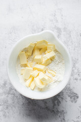 pieces of cold butter on flour in a white mixing bowl, organic butter on flour in a mixing bowl, process of making rough puff pastry