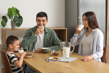 Little boy with his parents drinking milk at breakfast in kitchen