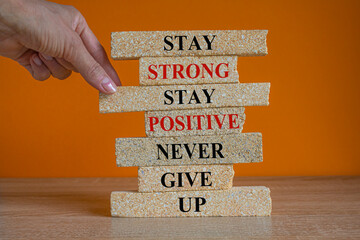 Brick blocks with concept words Stay strong stay positive never give up. Beautiful orange background. Copy space. Businessman hand. Motivational business never give up concept. - obrazy, fototapety, plakaty