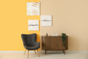 Grey armchair and wooden cabinet near colorful wall with different paintings