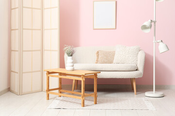 Light wooden coffee table with sofa, dressing screen and floor lamp near pink wall