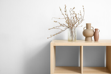 Vase with tree branches on wooden cabinet near white wall