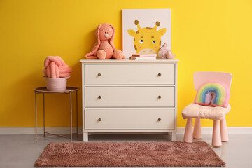 White chest of drawers with toys in children's room near yellow wall