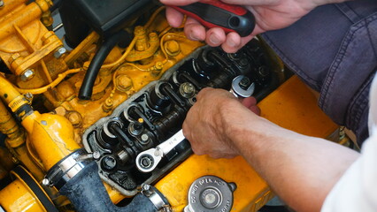 Engine of a boat that moves on diesel fuel. Adjusting the valves and maintenance on the yellow engine block that provides propulsion with horsepower by driving the propeller shaft.