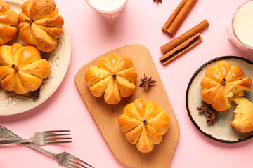 Plates and wooden board with pumpkin shaped buns on pink background