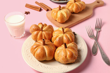 Tasty pumpkin shaped buns and glass of milk on pink background