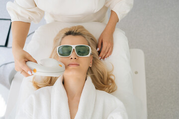 Closeup high-angle view of young woman client in protective glasses getting photo rejuvenation...