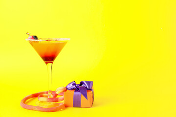 Glass of tasty Margarita cocktail for Halloween and gift box on yellow background