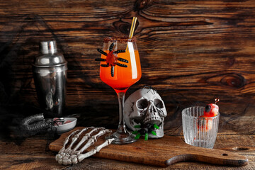 Glass of tasty Margarita cocktail for Halloween with skeleton hand and skull on wooden background