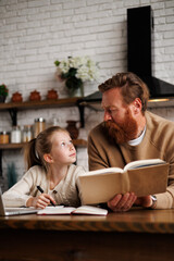 Fototapeta premium Father talking to daughter while holding book near laptop during internet-based learning in kitchen at home