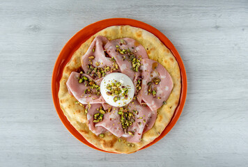 A piece of a traditional pizza of the Roman tradition, with Mortadella of Bologna, mozzarella cheese and Pistacchio grains, vision from above on wooden table 