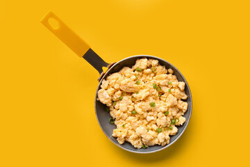 Frying pan of tasty scrambled eggs on yellow background