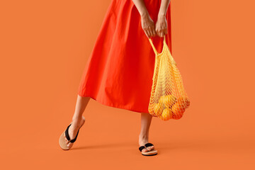 Beautiful woman in summer clothes and with eco bag on orange background