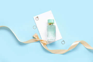 Perfume bottle, rings, greeting card and golden ribbon on blue background