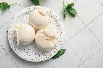 Plate of tasty Burrata cheese with basil on white tile background