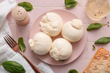 Plate of tasty Burrata cheese with basil on pink tile table