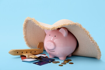 Piggy bank with wicker hat, wooden toy airplane and credit cards on blue background. Concept of...
