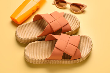 Female stylish flip flops with sunscreen cream and sunglasses on yellow background