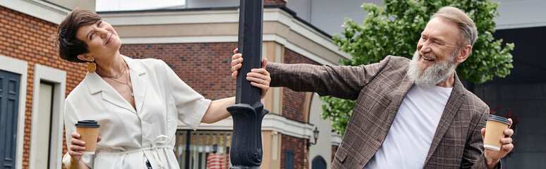 happy senior couple holding coffee to go, standing near street lamp, man and woman, romance, banner