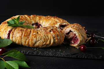 freshly baked cherry strudel on dark background with cutting piece. mint and almond and fresh cherries at the background