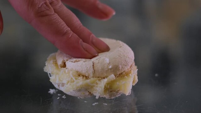 fingers press on vanilla coconut delicious macaroons female fingers break dessert. pierce a hole in the delicate structure of almond dough