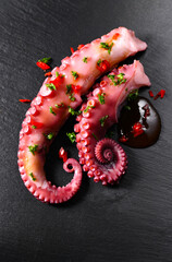 Octopus serving with vegetables, sea food. Freshly boiled curved octopus tentacles dish on a dark stone slate plate, Asian, Mediterranean cuisine, dinner. Restaurant menu, vertical image