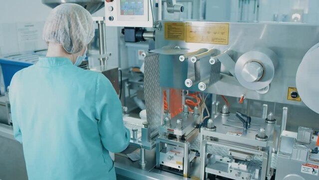 4K Blister Packing Machine. Woman works at the workplace. Tablet pharmaceutical blister packaging machine in supplement drug manufacture. Pharmaceuticals production line